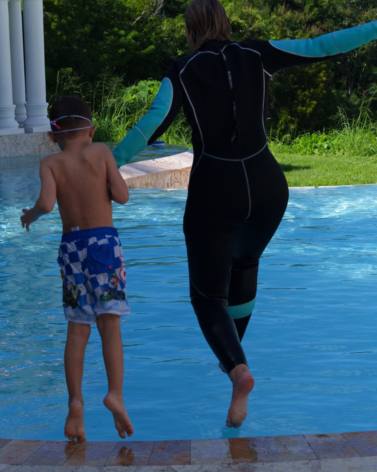 Instructor and a young swimmer jumping into the pool together, hand in hand