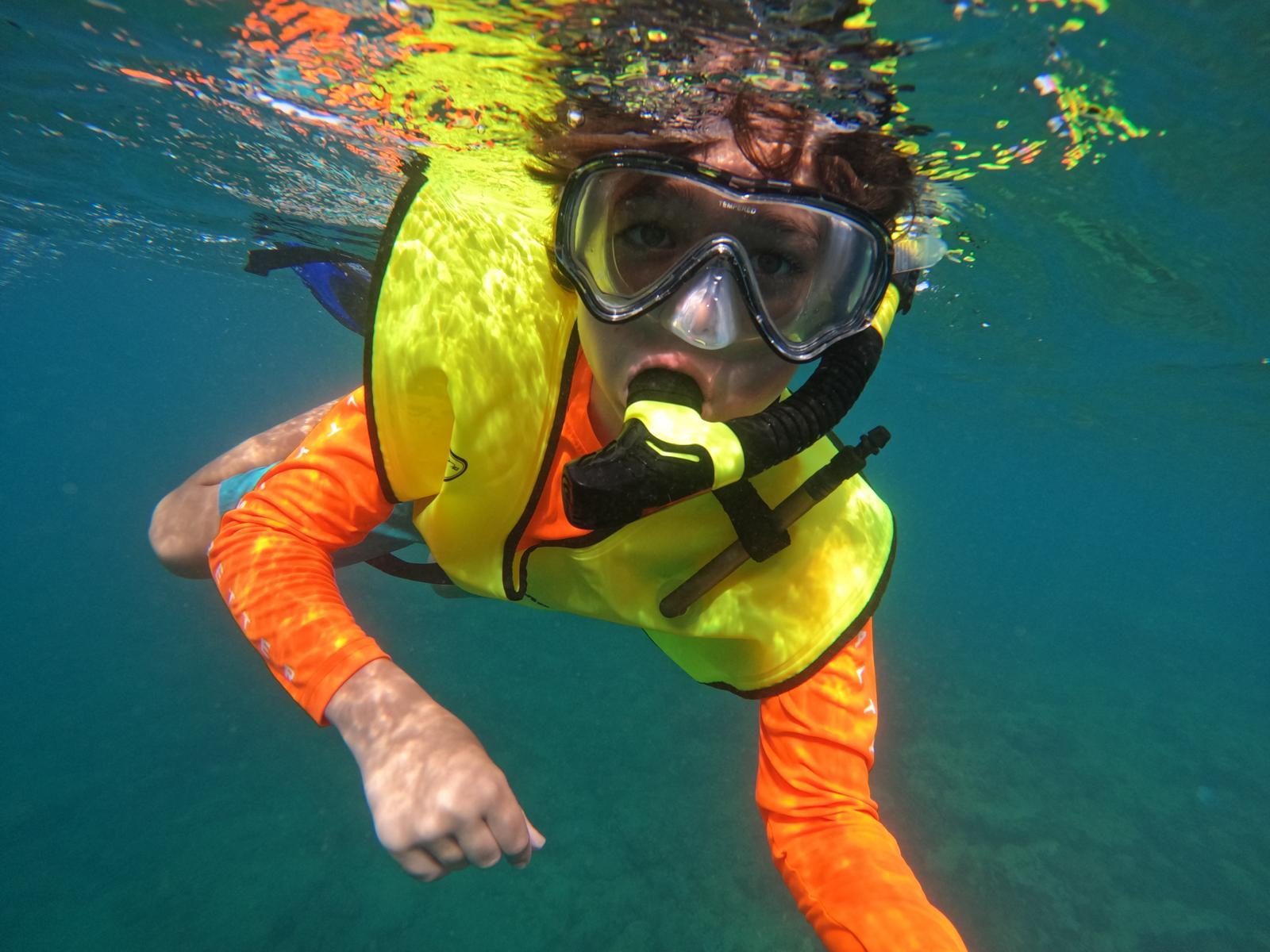 A young guest in mask and safety vest snorkeling at the surface