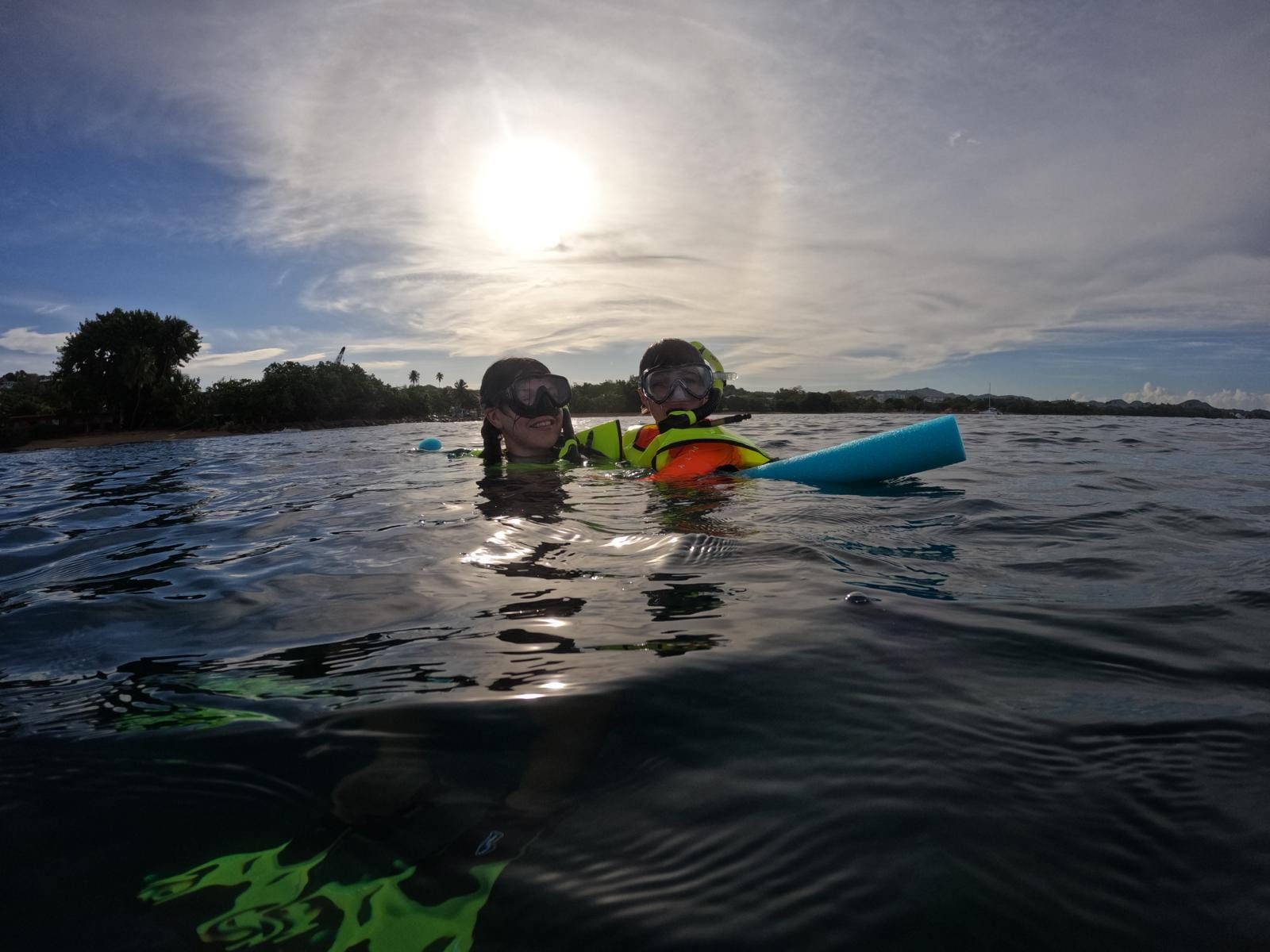 Two snorkelers at the surface with the Rincón shoreline and evening sun behind them