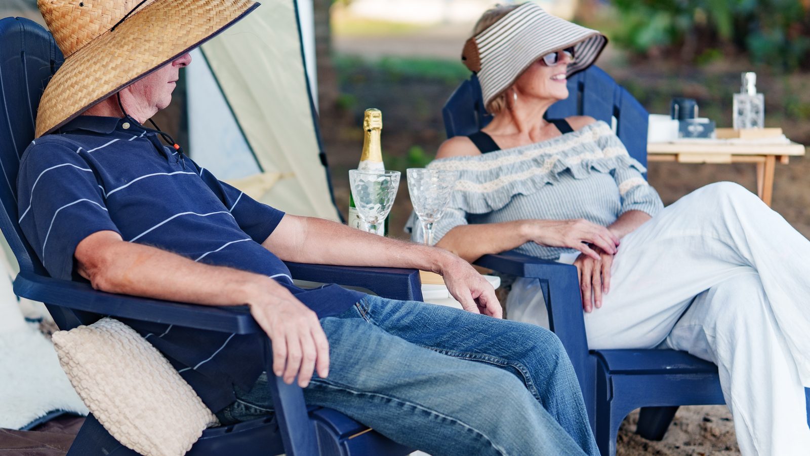 A couple relaxing in chairs beside the tent with glasses and a bottle on ice