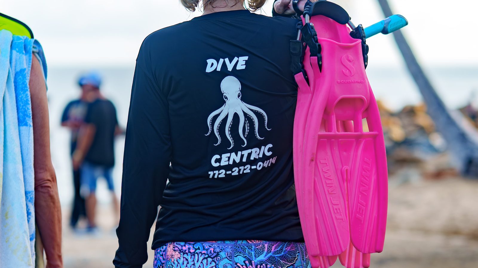A Dive Centric guide walking to the shore entry carrying fins and flotation gear
